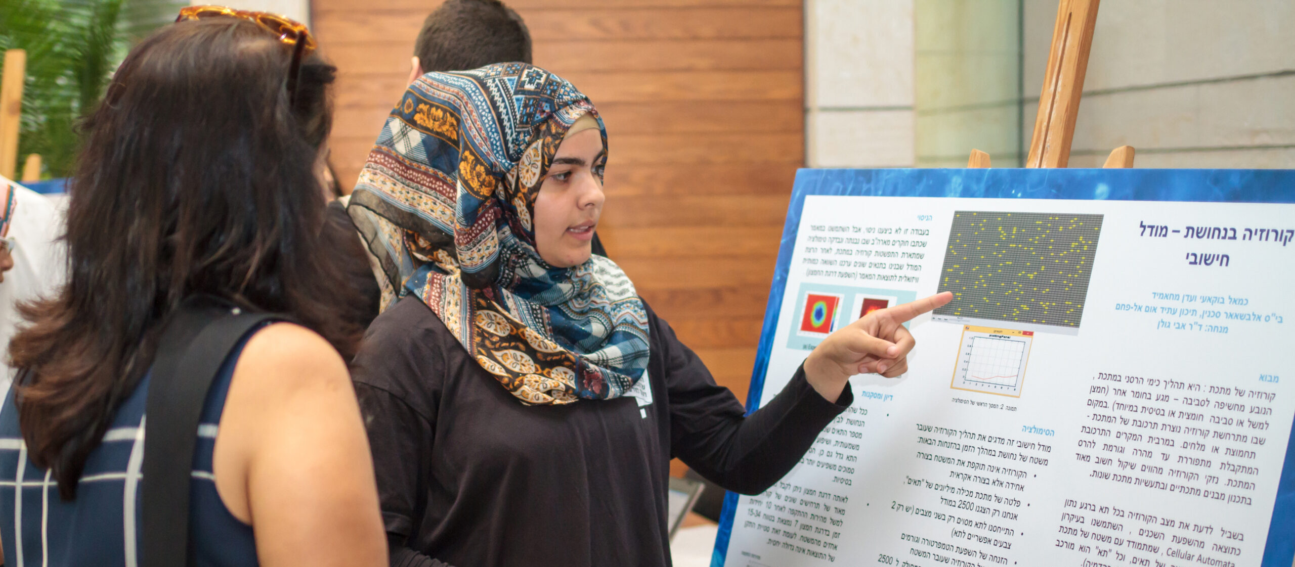 A student presenting a research poster to two women